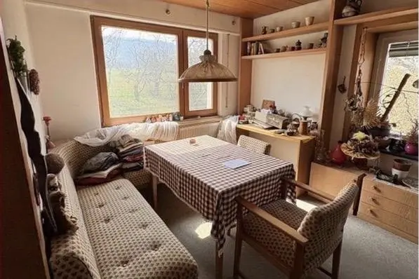 Möbliertes Wohn- und Esszimmer vor der Entrümpelung: Esstisch, Sitzbank, Sessel und volle Regale.