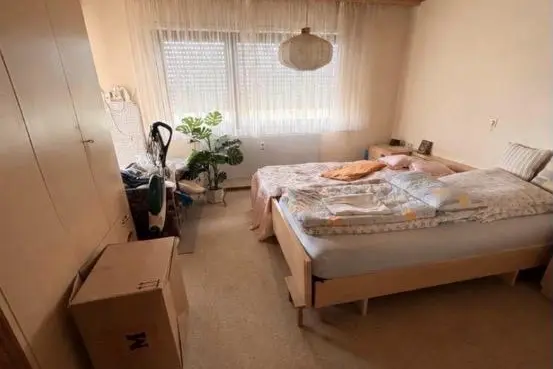 Schlafzimmer eines aufzulösenden Haushalts mit Bett, Schrank und bereitstehenden Umzugskartons.