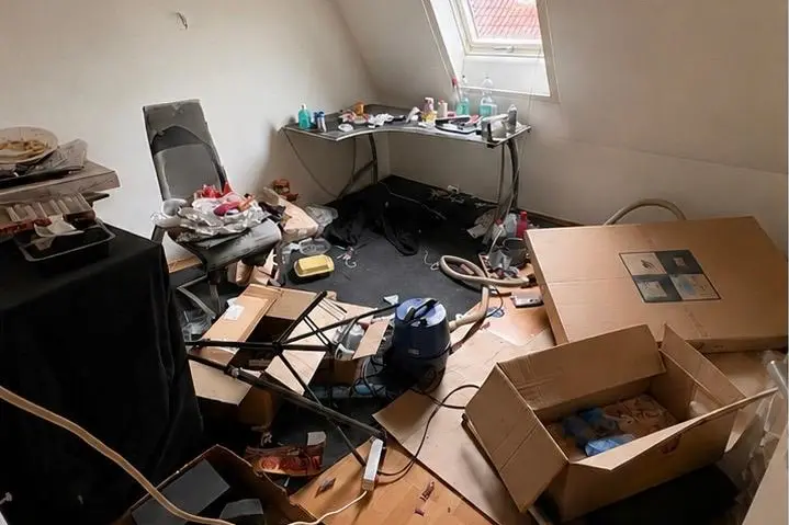 Stark zugestelltes Dachzimmer mit Kartons, Hausrat und Unrat auf dem Boden.